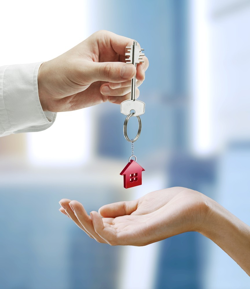 Man is handing a house key to a woman.Key with a keychain in the shape of the house. Image of a Man handing a house key to a woman.Key with a keychain in the shape of the house.